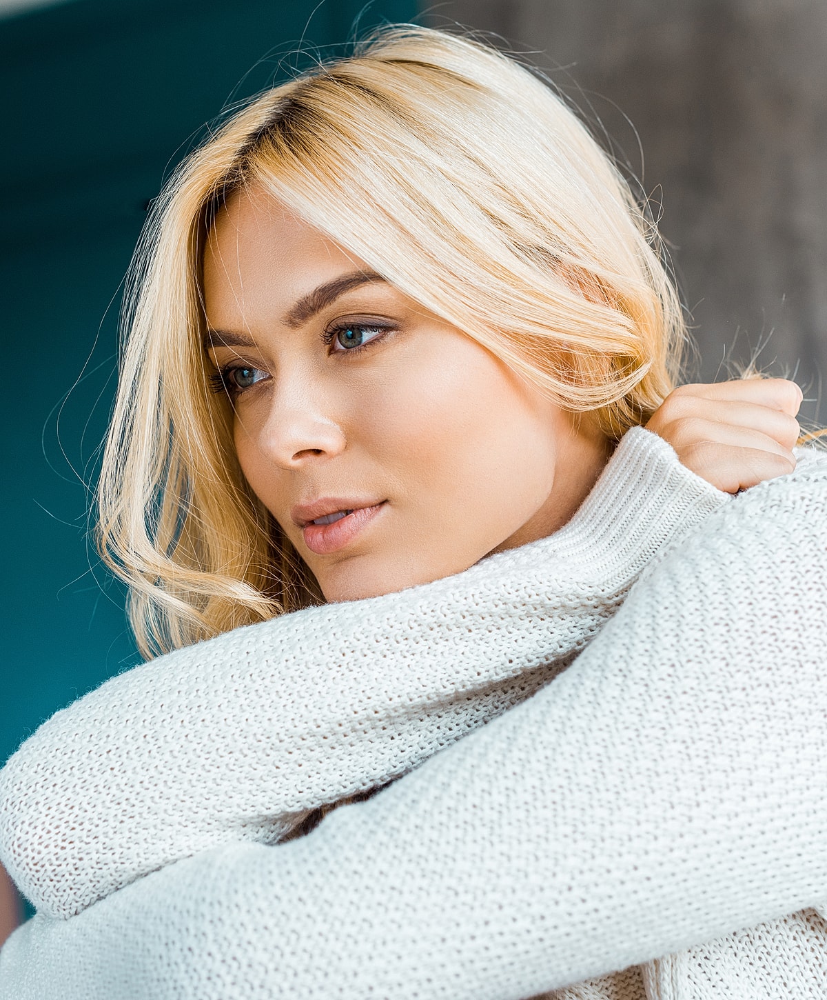 Blonde woman in cozy sweater, thoughtful expression.